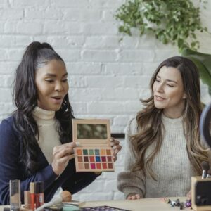 Young diverse ladies recording vlog about makeup products on smartphone