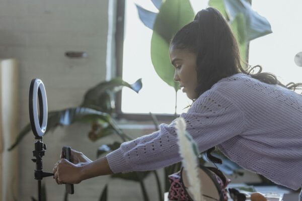 Young ethnic woman setting up smartphone before filming blog